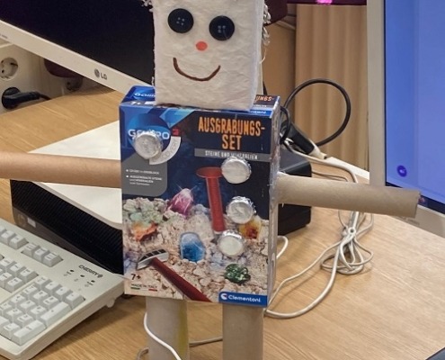 eine aus verschiedenen Materialien wie Papprollen und Kartons zusammengebaute Figur, an der Kabel befestigt sind